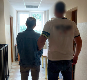 policjant kryminalny prowadzi zatrzymaną korytarzem komendy