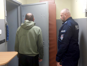 Policjant prowadzi zatrzymanego do celi