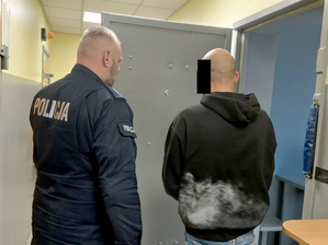 Policjant prowadzi zatrzymanego do celi