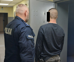 Policjant prowadzi zatrzymanego do celi
