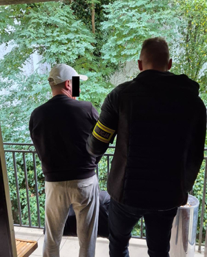 Policjant z zatrzymanym mężczyzną przed domem