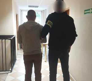 Policjant kryminalny prowadzi zatrzymanego korytarzem