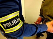 Policjant z opaską na ręku trzyma zatrzymanego