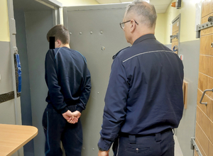 Policjant prowadzi zatrzymanego do celi
