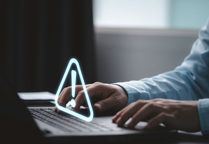 Osoba przed laptopem i znak ostrzegawczy