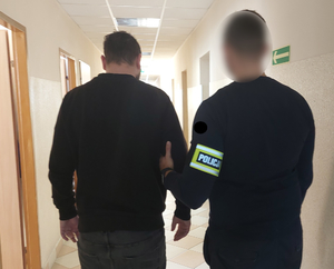 Policjant prowadzi zatrzymanego korytarzem komendy