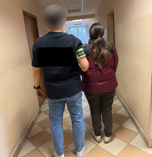 Policjant prowadzi zatrzymaną korytarzem komendy